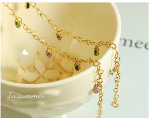 Detail of heart-shaped gold chain links and multi-colored rectangular gemstone charms