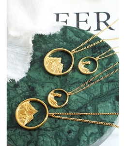 Detail of gold circular pendant necklaces with mountain and wave relief on green marble