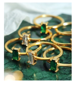 Detail of minimalist gold rings with emerald-cut green and white zircon on marble