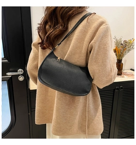 Side view of a sleek black baguette shoulder bag with gold hardware on a female model