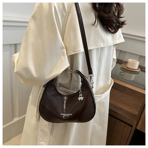Detail of burgundy crescent leather bag with metallic clover charm and silver hardware