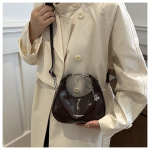 Detail of retro crescent bag in dark brown glossy leather with clover charm zipper