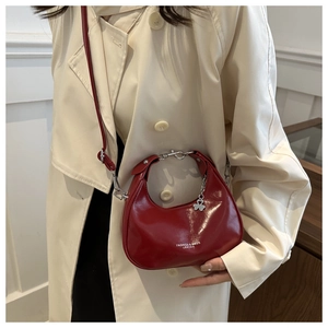 Detail of red crescent shoulder bag with silver hardware and clover pendant on beige coat