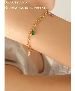 Detail of gold-plated heart chain bracelet with emerald, violet, and clear rectangular gems