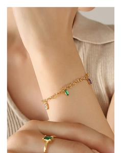 Close-up of heart-link gold bracelet and matching colorful gemstone rings on a model
