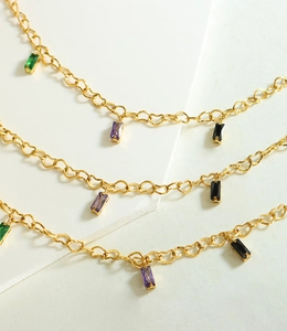Detail of gold heart-link bracelet with emerald, purple and black zircon charms