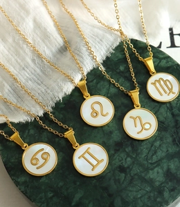 Détail des colliers zodiaque plaqués or 18 carats avec nacre sur marbre vert