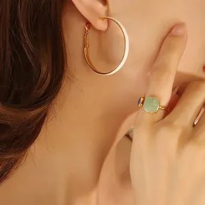 Elegant gold hoop earrings with white enamel and green gemstone ring on a model