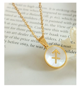 Détail du collier Sagittaire plaqué or 18K avec nacre blanche sur un livre ouvert