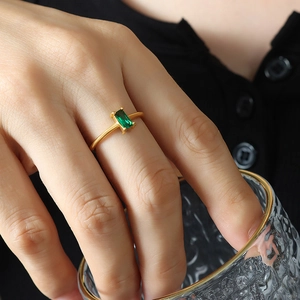 Gold minimalist ring with emerald green zircon stone worn by model holding glass