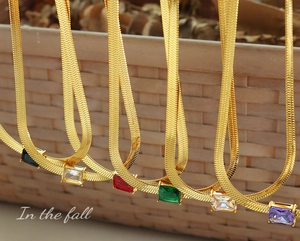 Detail of multicolored zircon pendants on golden herringbone snake chains against a rustic background