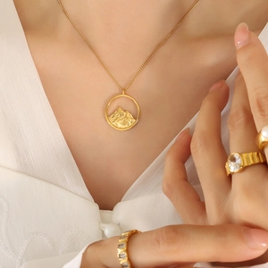 Minimalist gold necklace with mountain relief pendant and matching rings on model