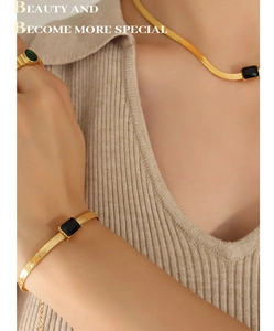 Close-up of golden blade chains with black rectangular stones and matching ring on model