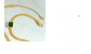 Detail of a gold snake chain necklace featuring a square green emerald-cut gemstone inlay