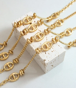 Primer plano de cadena dorada con eslabones y anillos trenzados sobre piedra blanca