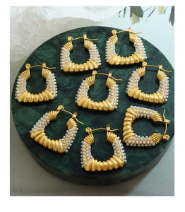 Close-up of gold ribbed U-shaped hoop earrings with pearls on marble plate