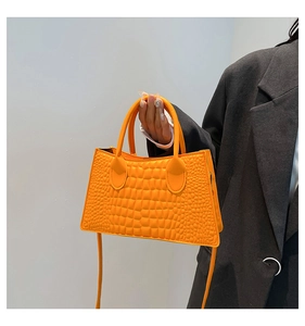 Detail of bright orange crocodile pattern tote bag held by a model in a grey blazer