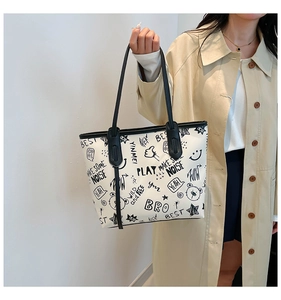 Detail showing street graffiti print and black contrast handles on the white tote bag