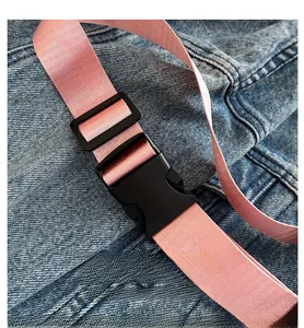 Detail of pink woven strap with black buckle and blue denim fabric of shoulder bag