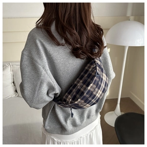 Detail of plaid chest bag with dual zippers shown on model in a minimalist setting