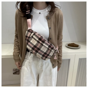 Detail of plaid crossbody bag featuring pink woven strap and geometric zipper charm