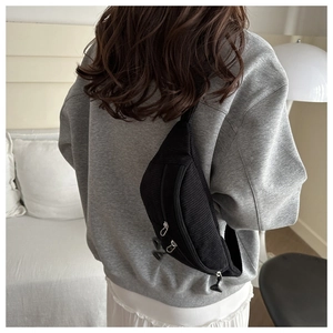 Close-up of black corduroy crossbody bag with multiple zippers shown on a model's back
