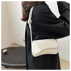 Detail of white minimalist shoulder bag with asymmetrical curved flap and knotted strap