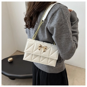 Détail d'un sac bandoulière blanc matelassé avec boucle papillon dorée et chaîne