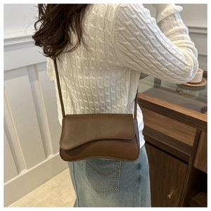 Sac bandoulière en cuir marron avec rabat asymétrique porté sur un pull blanc