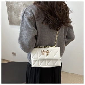 Détail d'un sac à bandoulière matelassé blanc avec nœud doré et bandoulière chaîne