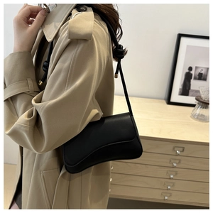 Close-up of minimalist black leather shoulder bag with unique knotted strap and metal seal