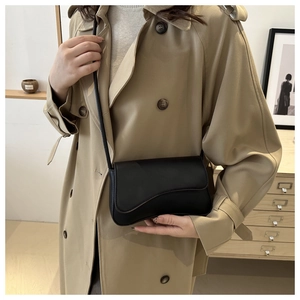 Close-up of minimalist black leather crossbody bag styled with a tan autumn trench coat