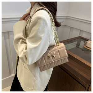 Détail du sac carré matelassé beige avec décoration papillon dorée et bandoulière chaîne
