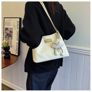 Detail of cream waffle texture shoulder bag with decorative tag and plush cloud pendant