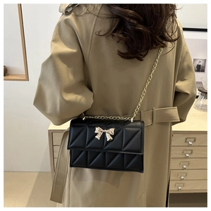 Détail du sac bandoulière matelassé noir avec fermoir papillon doré et chaîne en métal
