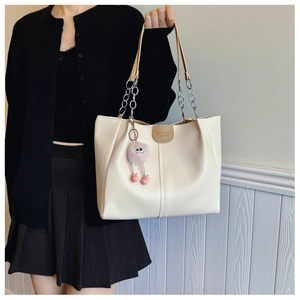 Detail of cream tote bag with leather logo patch, chain strap and pink plush charm