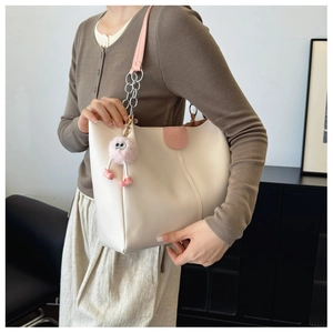 Detail of off-white tote bag with pink straps and cute plush monster pendant charm