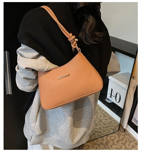 Brown underarm bag with wave texture and knotted strap shown on model shoulder