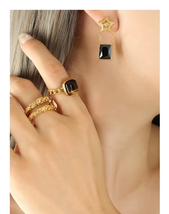 Détail de boucle d'oreille étoile avec pierre noire et bagues dorées sur modèle