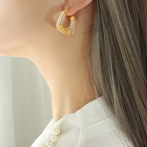 Gold U-shaped pearl earrings featuring twisted geometry texture on a model