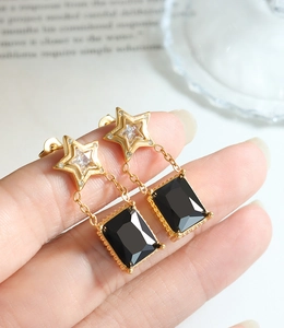 Détail de boucles d'oreilles étoile avec pierre noire rectangulaire et chaîne dorée