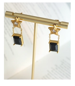 Détail de boucles d'oreilles étoile dorées avec pierres noires rectangulaires et chaînes