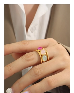 Detailed view of a wide gold ring featuring three colorful oval stones on a model
