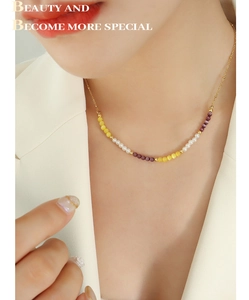 Détail d'un collier en perles dorées avec œil de chat jaune et pierres mauves sur modèle