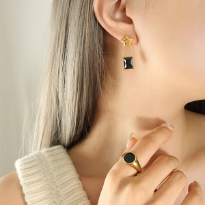 Parure boucles d'oreilles étoile dorée et bague pierre noire portée par un mannequin
