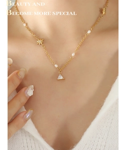 Dettaglio della collana dorata con zircone a triangolo, perle d'acqua dolce e ciondolo a stella