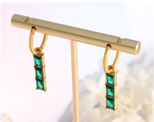Close-up of gold earrings with three emerald-green rectangular stones on a jewelry stand
