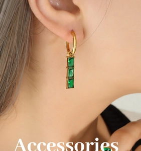 Close-up of gold-plated earrings featuring three emerald-green rectangular gemstones