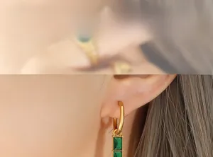 Close-up of gold titanium hoop earring featuring an emerald green rectangular gemstone pendant