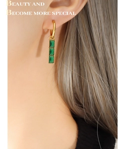 Detailed side view of a dangling gold earring featuring three vertical green zircon stones
